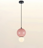 A modern pendant light with a matte black ceiling canopy and cord, featuring a large dusty pink glass globe shade with a smaller white globe bulb hanging below, set against a soft beige gradient background.
