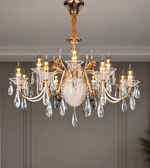 Gold-tone chandelier with curved decorative arms, candle-style bulbs, a sculptural central ornament, and clear faceted hanging drops.