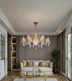 Luxury gold crystal chandelier suspended above a cream sofa in an elegant living room with neutral walls and warm interior lighting.