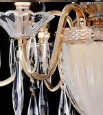 Close-up of an ornate chandelier with a polished gold-tone metal frame, clear faceted glass shades, and hanging crystal prisms against a dark background.