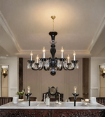 Black crystal chandelier with illuminated candle-style bulbs and hanging crystal accents above a formal dining table in an elegant interior.