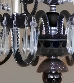A close-up of a black chandelier with clear faceted crystal drops and silver-toned metal details against a neutral indoor background.