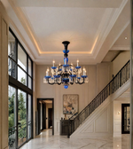 Blue and black crystal chandelier with illuminated candle-style bulbs displayed in a spacious luxury entrance hall with a staircase.
