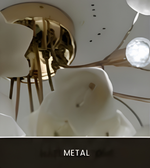 A close-up of a modern ceiling light fixture with sculptural white calla lily-shaped shades and metallic bronze arms, viewed from below against a white ceiling. A dark banner at the bottom reads 'METAL'.