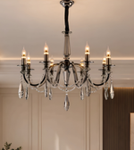 Front view of an illuminated chrome crystal chandelier featuring curved arms, sparkling crystal garlands, and hanging teardrop pendants.
