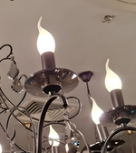 Close-up of a decorative chandelier showing illuminated flame-shaped bulbs, curved black-finished arms, reflective holders, and crystal embellishments.