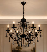 Close-up of a black ornate chandelier featuring curved metal arms, decorative crystal drops, and illuminated candle-shaped bulbs.