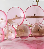 Close-up of a pink glass disc chandelier featuring translucent circular discs, pink edges, and golden decorative fittings.
