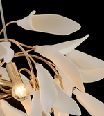 A close-up of a modern chandelier featuring frosted white glass calla lily-shaped shades on a gold-toned metal frame, with a glowing light bulb visible against a solid black background.