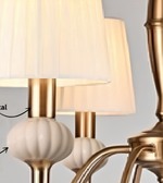 Close-up of a gold chandelier featuring ivory pleated shades, decorative ribbed accents, and curved metal arms.
Copy alt text