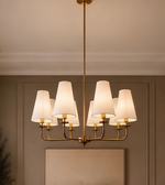 Close-up of a gold-tone eight-light chandelier featuring curved metal arms and cream tapered shades.