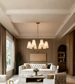 Gold eight-light chandelier with cream tapered shades in an elegant living room with neutral furnishings and wall panelling.