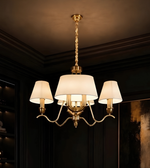 A three-light brass chandelier with white drum shades hanging from a twisted chain in a dark, elegant room.