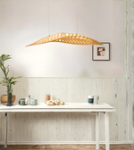Modern wooden leaf pendant light hanging above a dining table in a minimalist interior