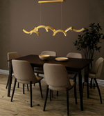 Sculpted golden wave LED dining pendant light above a modern dining table interior