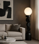 Black sculptural floor lamp with opal globe beside modern sofa in living room