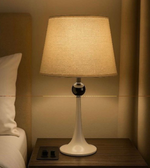 Table lamp on a nightstand next to a bed with soft lighting