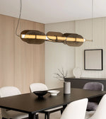 Modern gold linear pendant light over black dining table with minimalist decor