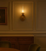 Modern brass wall sconce glowing in elegant dining room with wood cabinet and paneling