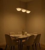 Three-dome frosted glass pendant light suspended above an elegant dining table with beige seating