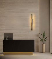 Linea vertical wall light with marble finish glowing softly on a beige wall near modern reception setup