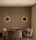 Round marble-effect LED wall light glowing on wooden panel wall in a modern dining room.
