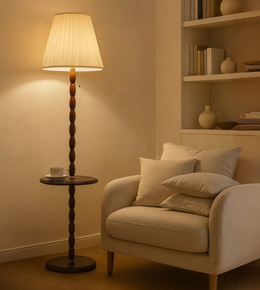 Scandinavian wooden floor lamp with warm fabric shade and built-in table placed beside a beige armchair.