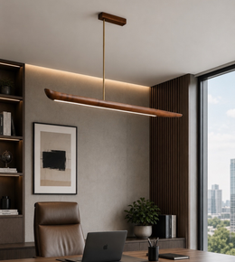 A modern linear pendant light with a warm wood-grain finish and a slim brass rod hangs over a office desk. 