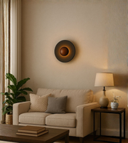 Black and bronze round wall lamp used as stylish décor above living room sofa.