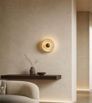 Modern round wall sconce with warm glowing inner core installed above floating wood shelf.
