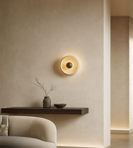 Modern round wall sconce with warm glowing inner core installed above floating wood shelf.