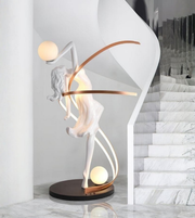 Illuminated dancer sculpture floor lamp with glowing spheres in a luxury modern interior near marble staircase