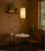 Warm cylindrical pendant light hanging above a small café table against brick wall.