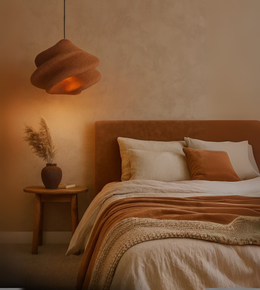 Rust/Stone red-colored sculptural foam pendant light with wavy design hanging over a warm-toned bedroom.