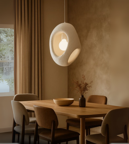 Loop-shaped white foam pendant light glowing softly over a wooden table.