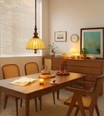 Solid wood and fabric pendant light with copper body finish, hanging above a wooden dining setup, casting a warm ambient glow.