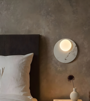 White marble disc wall light with frosted globe mounted beside bed
