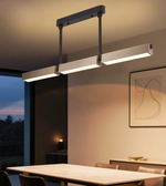 Modern triple linear LED pendant light with champagne-toned rectangular light modules and black adjustable suspension above a contemporary dining table.