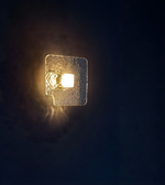 Clear textured glass square wall light with warm illuminated center mounted on indoor wall