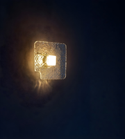Clear textured glass square wall light with warm illuminated center mounted on indoor wall
