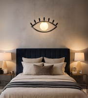 Visionary designer pendant in eye shape with glowing orb diffuser above a bed in a luxury bedroom.