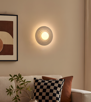 Modern ripple ring round wall light in beige tone illuminating a cozy living room interior