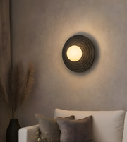 Ripple ring round wall lamp in dark finish providing warm ambient light in a stylish interior setting
