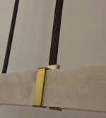 Modern linear pendant light with marble-effect rectangular diffuser, champagne-gold accents, and black suspension above a luxury dining table.