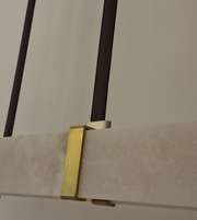 Modern linear pendant light with marble-effect rectangular diffuser, champagne-gold accents, and black suspension above a luxury dining table.