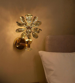 Ray Bloom crystal floral wall light with gold finish beside beige headboard.