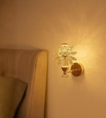 Bloom Glow crystal floral wall light with gold finish beside a beige bed.