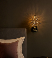 Bloom Glow crystal floral wall light with gold finish beside a bed.