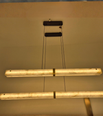 Close-up view of modern marble-effect linear pendant lights featuring illuminated cream diffusers, subtle veining, gold detailing, and black suspension cables.
