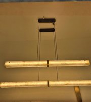 Close-up view of modern marble-effect linear pendant lights featuring illuminated cream diffusers, subtle veining, gold detailing, and black suspension cables.
